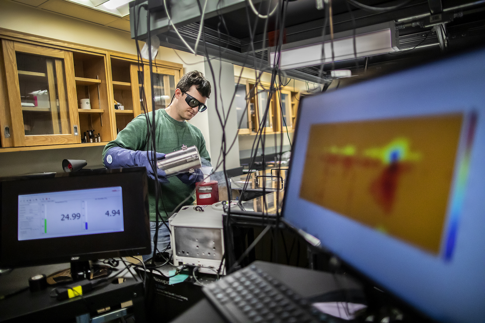 a person inside of a lab pouring liquid nitrogen into a container with a computer screen in the foreground