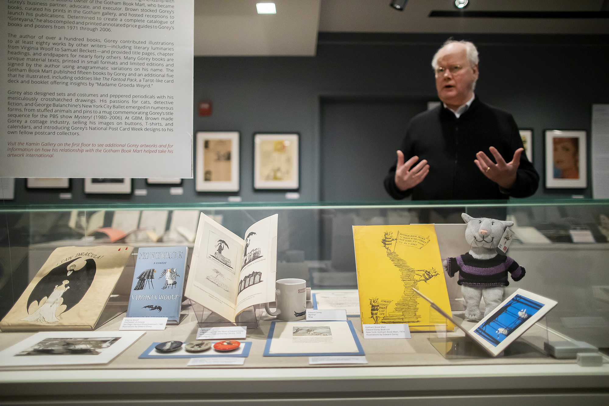 Librarian standing behind museum display case holding several books and illustrations.