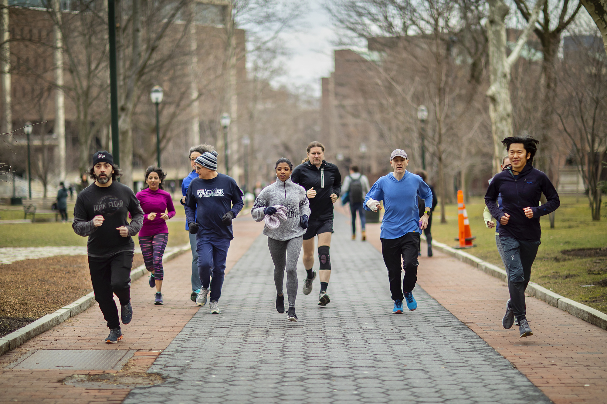 A group of runners makes their way down a wide path framed by trees and buildings.
