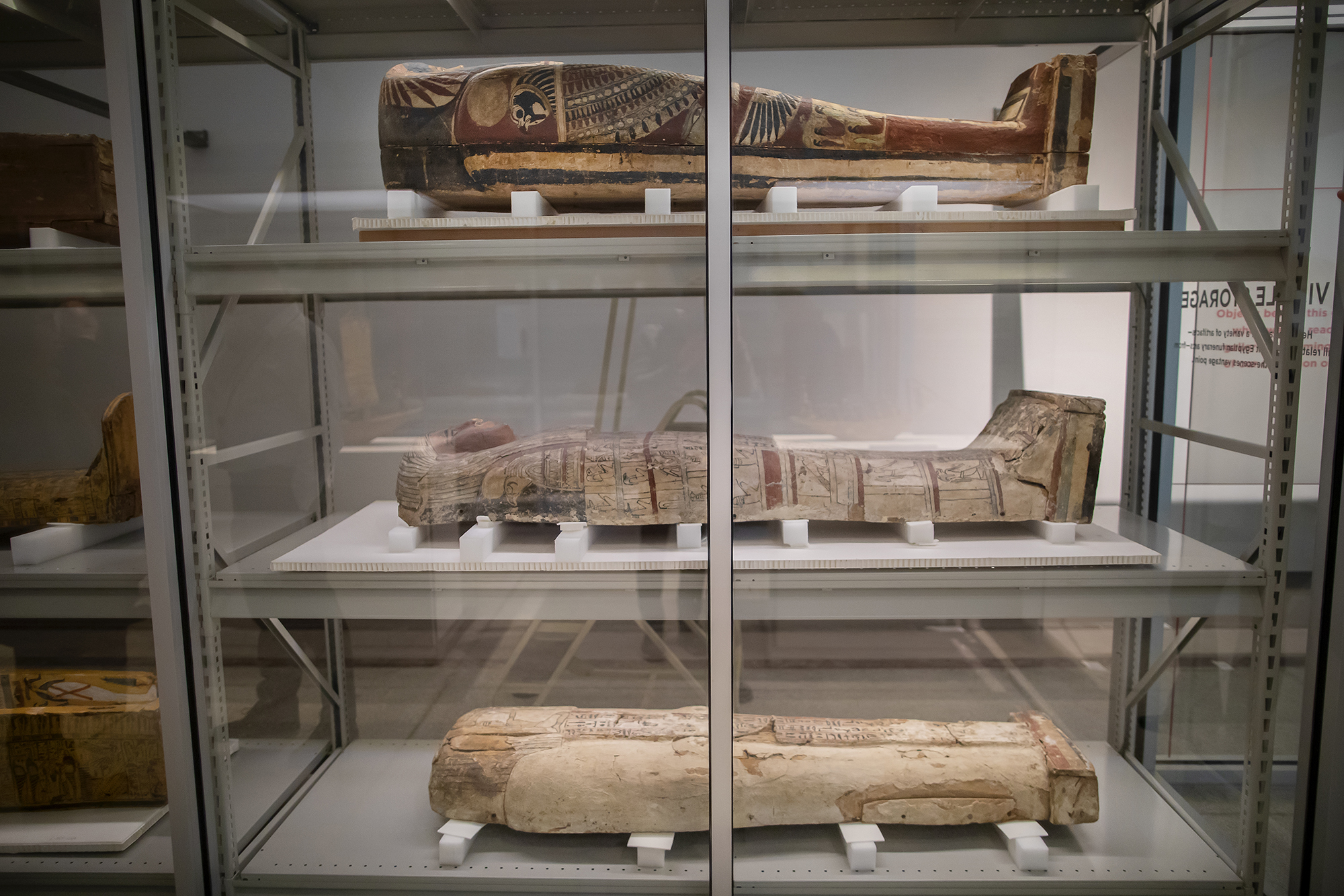 Three Egyptian coffins are displayed on shelves.