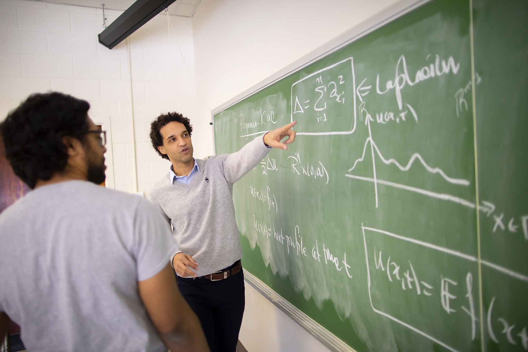 a student and a professor looking at equations on a chalk board