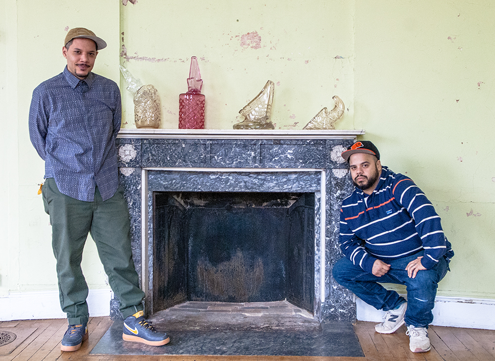 Artists pose with glass sculptures atop a fireplace mantle 