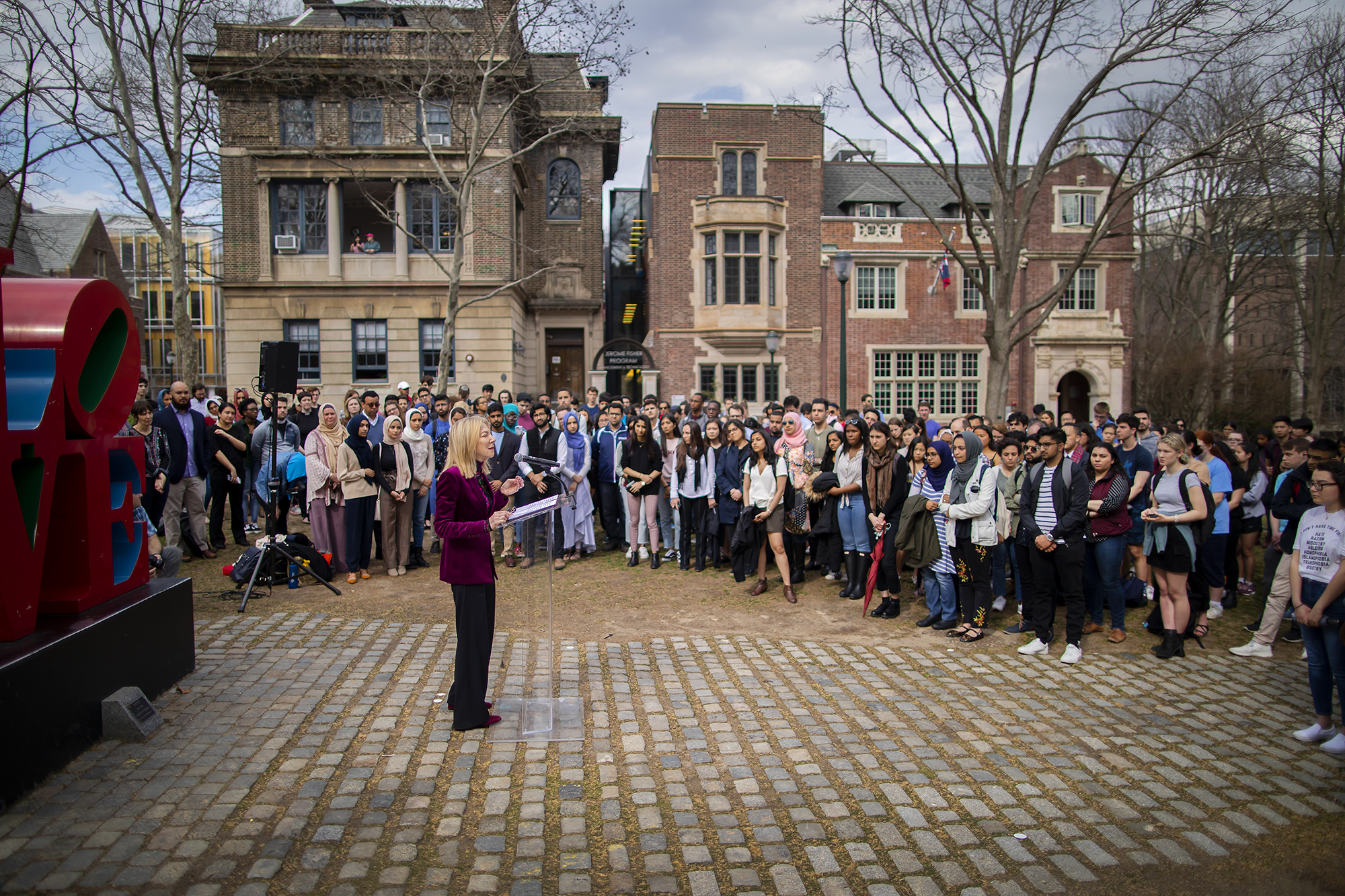 Dr. Gutmann stands and addresses a crowd in front of the LOVE statue on campus outside in daylight
