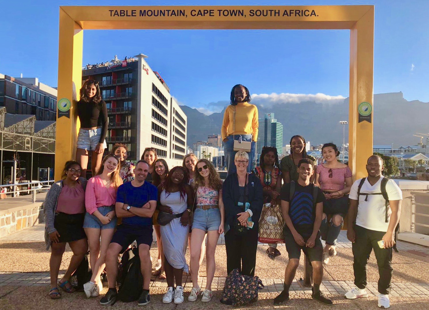 Group of students and professor gathered at monument with mountain in back.