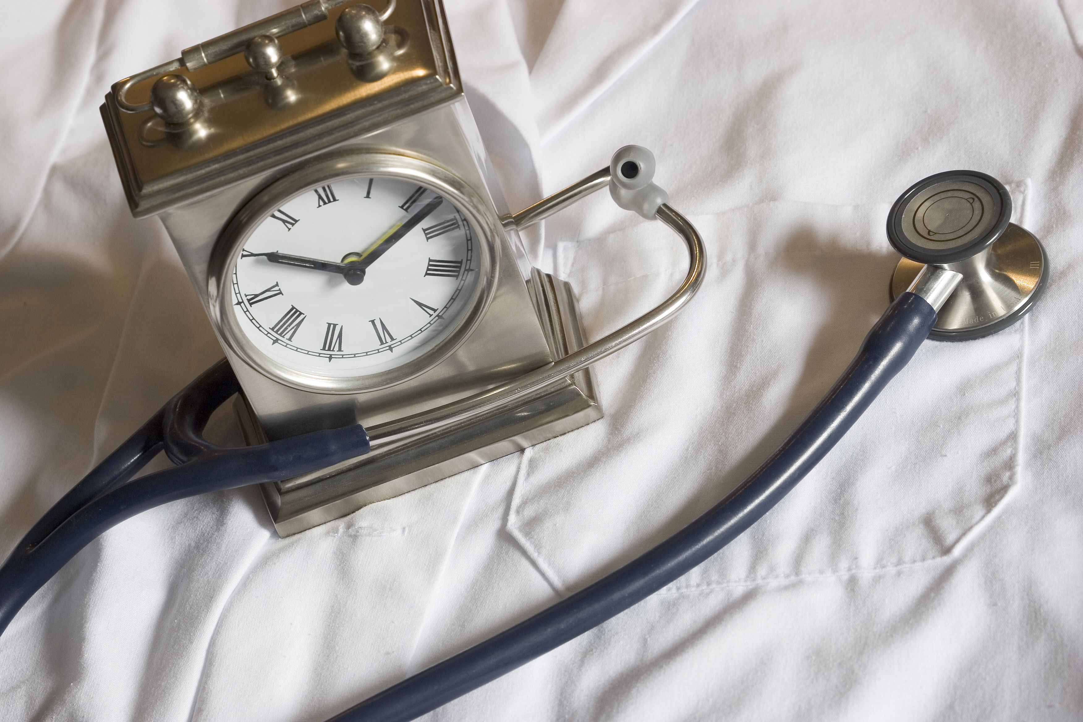 A clock and a stethoscope on top of a white lab coat. 