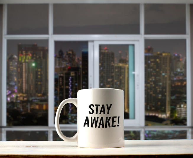 mug on windowsill overlooking the city at night that reads Stay Awake!