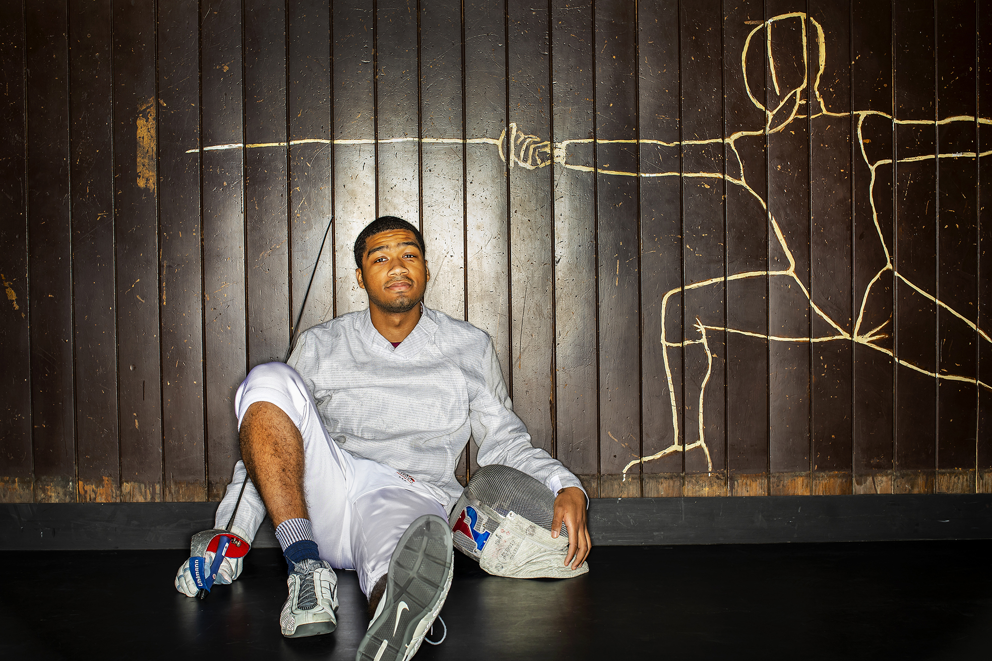 Fencer Julian Merchant poses seated with his sword and mask in Hutchinson Gym.