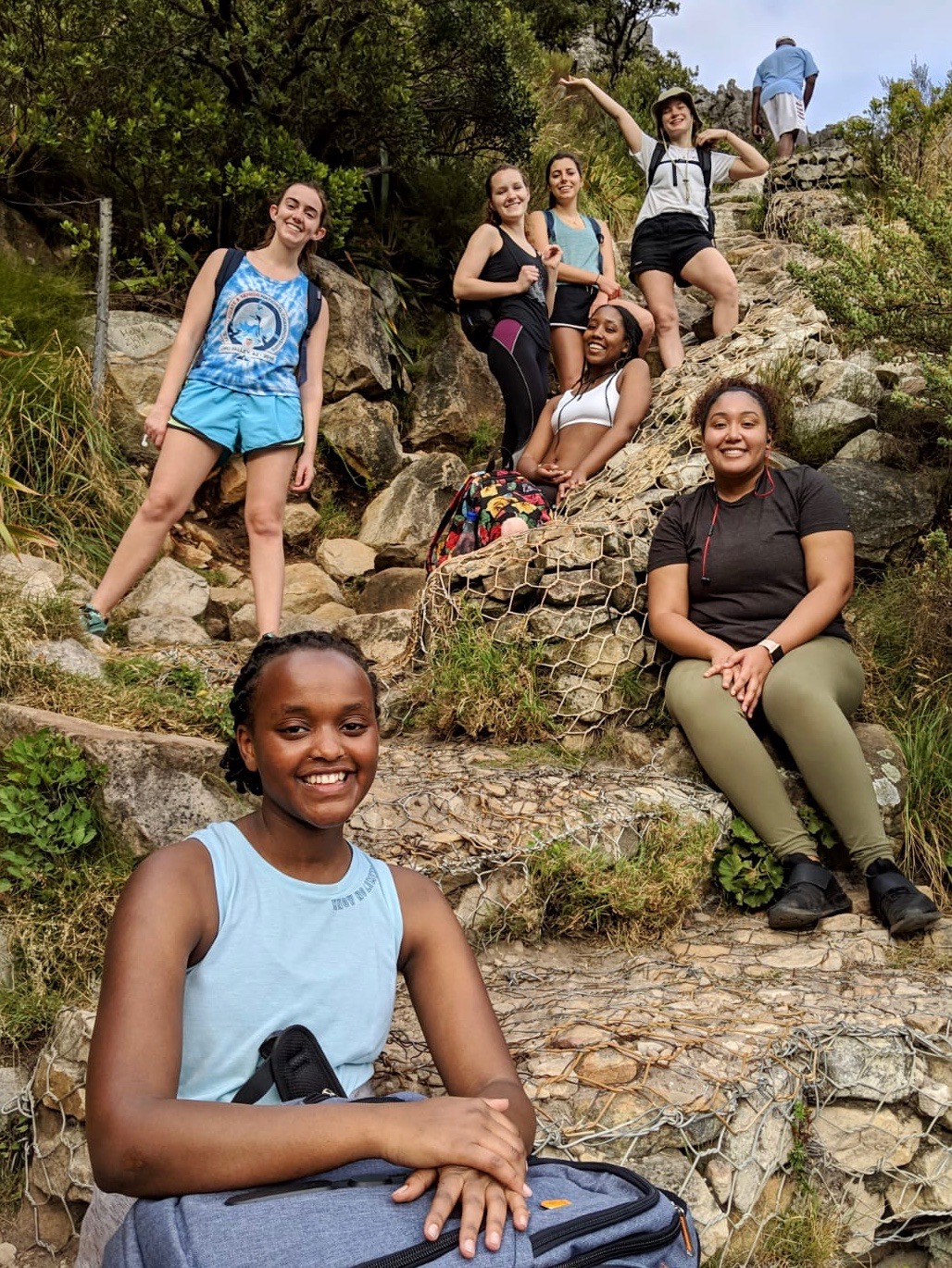 Six students climbing a rocky mountain turn to look at the camera. 