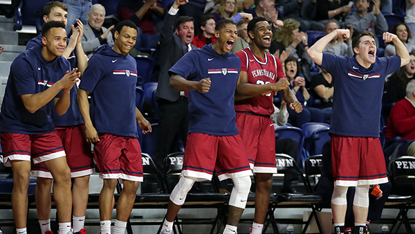 members of the Penn Quakers basketball team stand and cheer from the sideline
