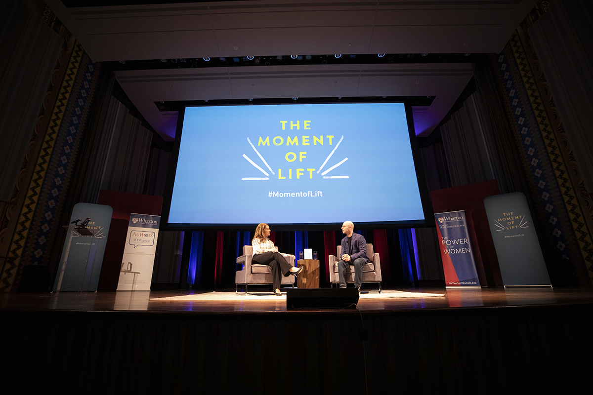 Melinda Gates and Adam Grant on stage under a large projected image reading The Moment of Lift