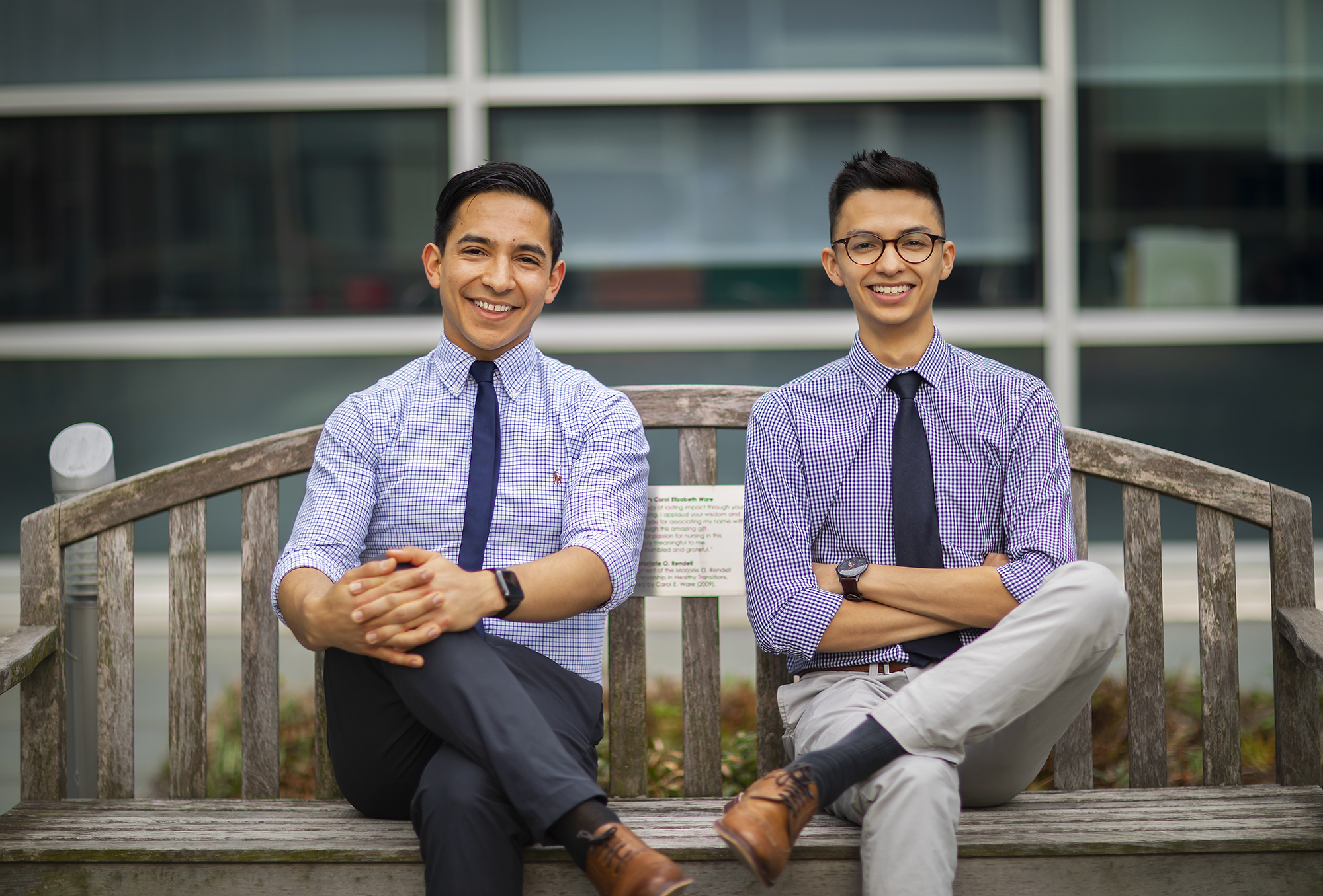 Two men sitting cross-legged on a wooden bench. 