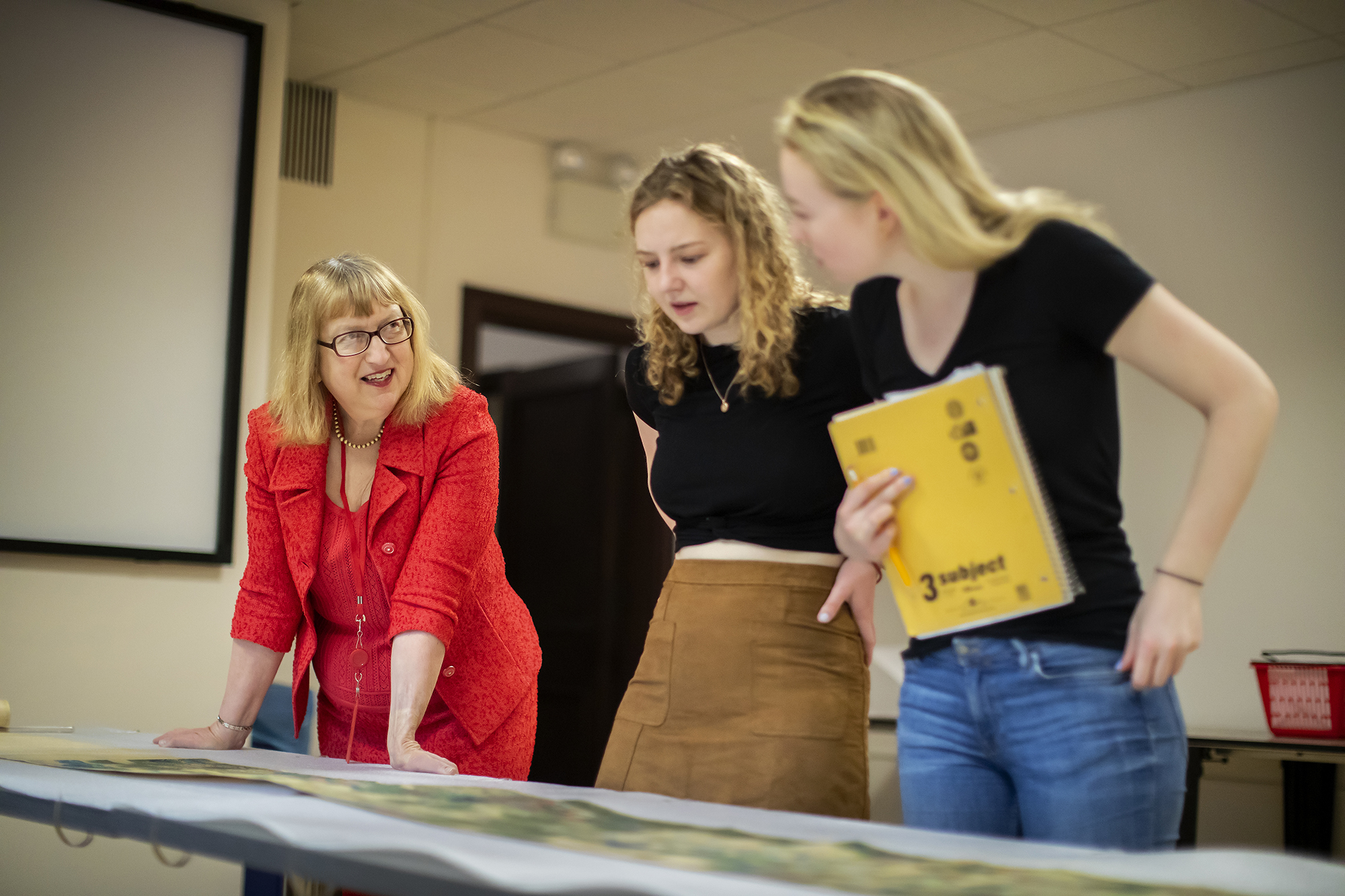 Professor speaking to two students while looking at the Chinese scroll. 