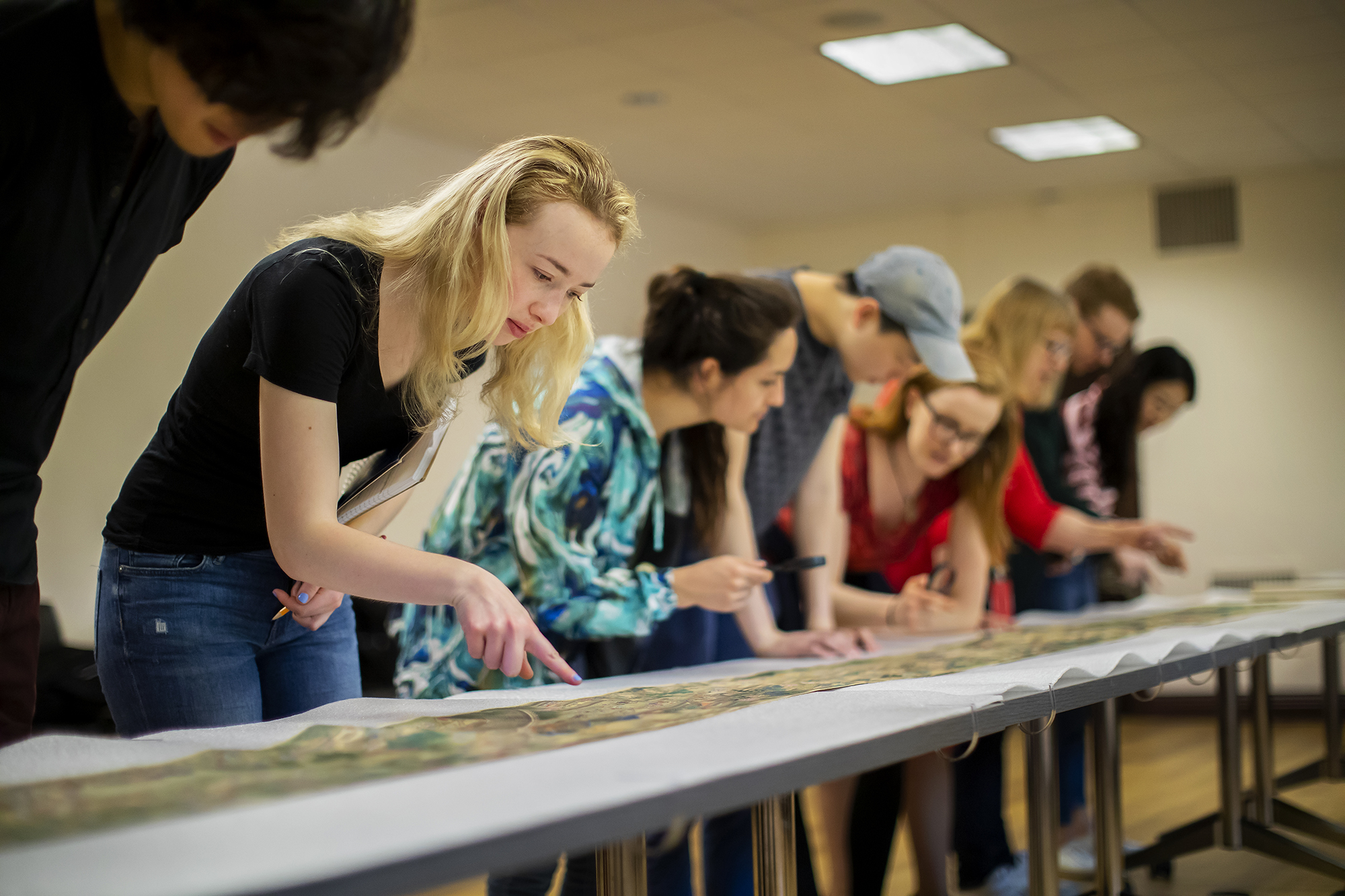 Students studying Chinese scroll unrolled on a series of tables. 