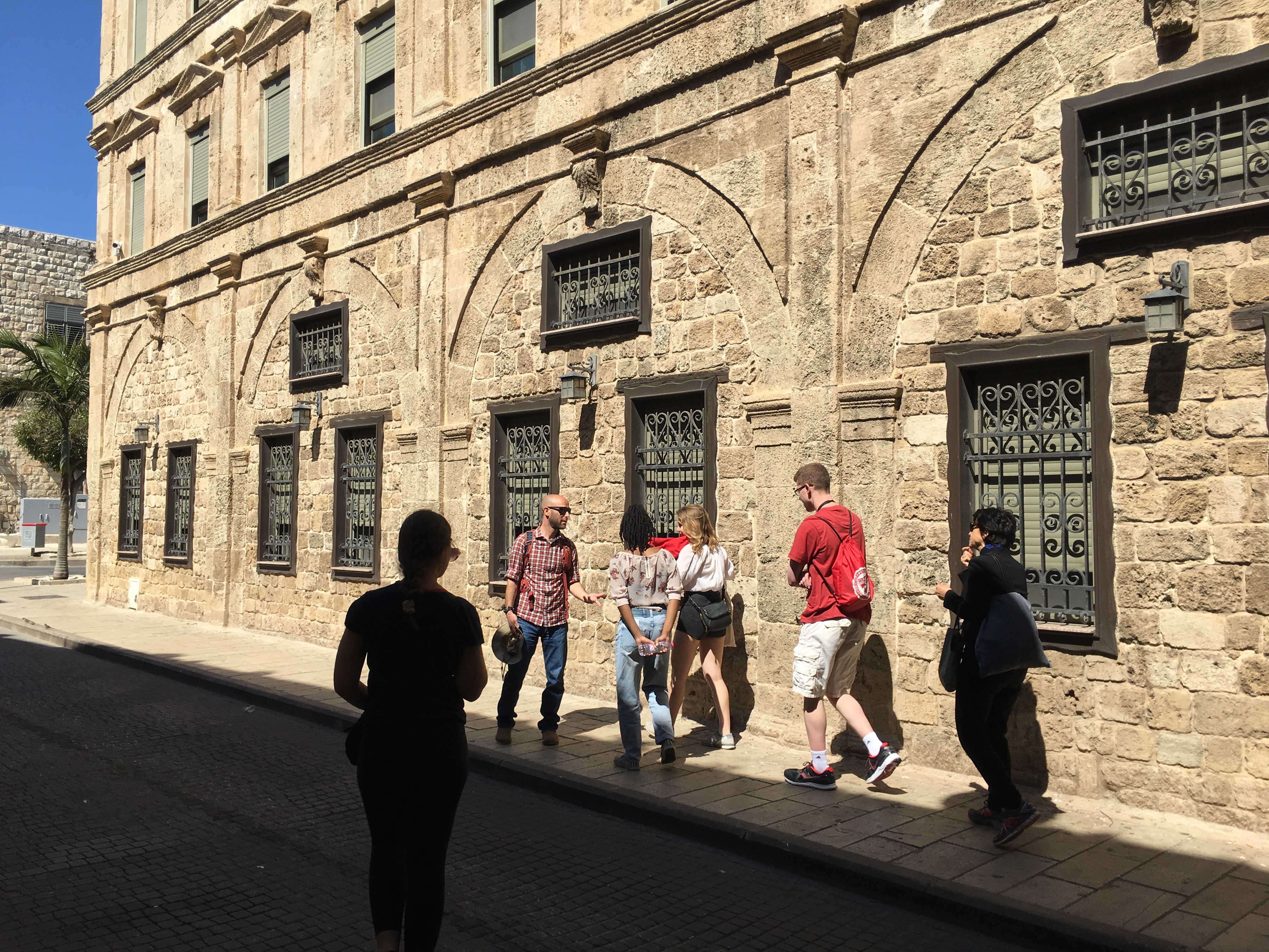 A group of people walking in front of a stone building in Haifa, Israel.