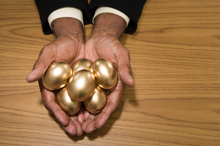 outstretched hand holding several golden eggs on a table