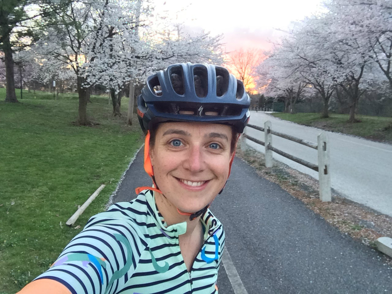 'Selfie' of a person wearing a bike helmet with cherry trees and a sunset in the background