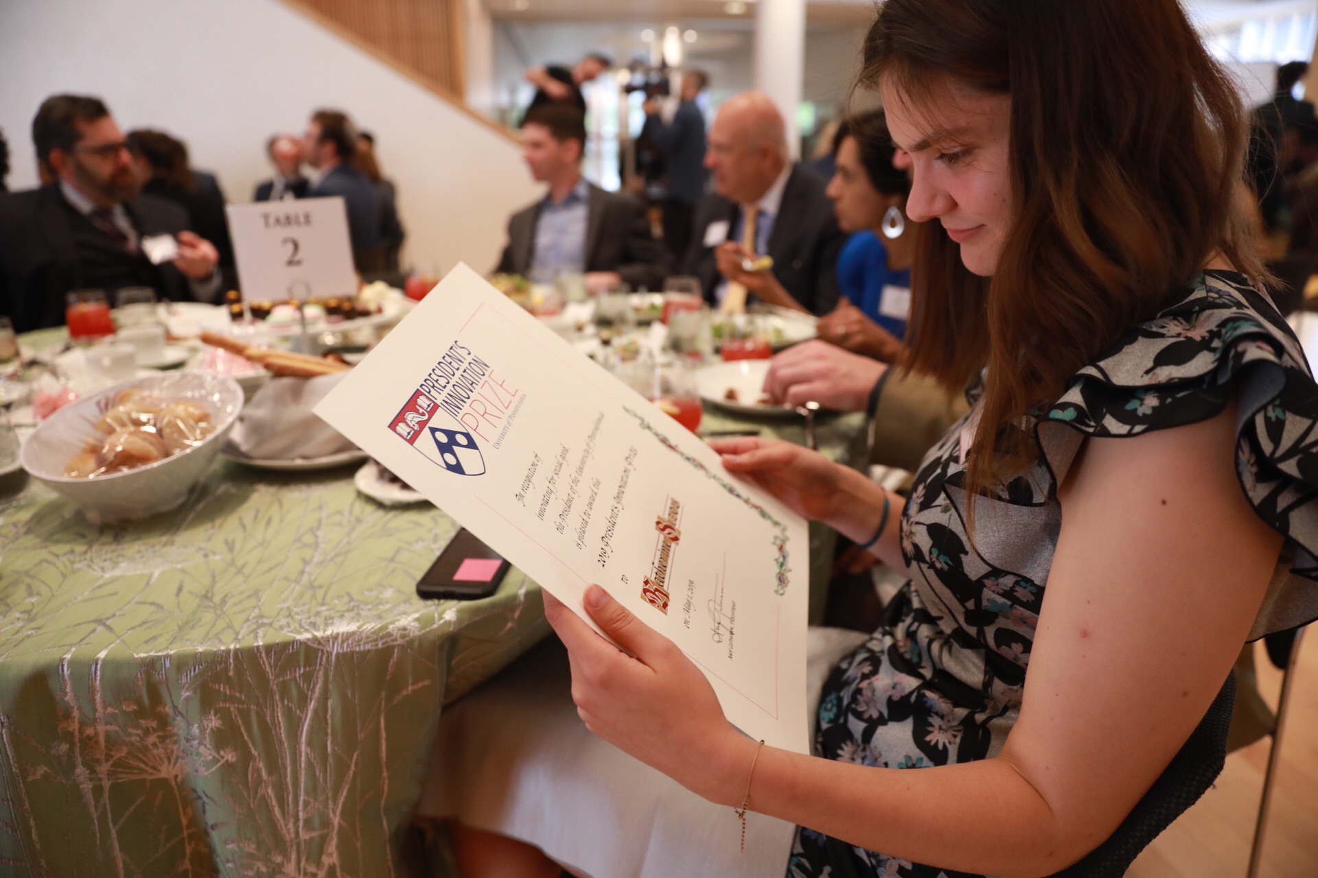 Katherine Sizov sits at a luncheon table, looking at her award certificate.