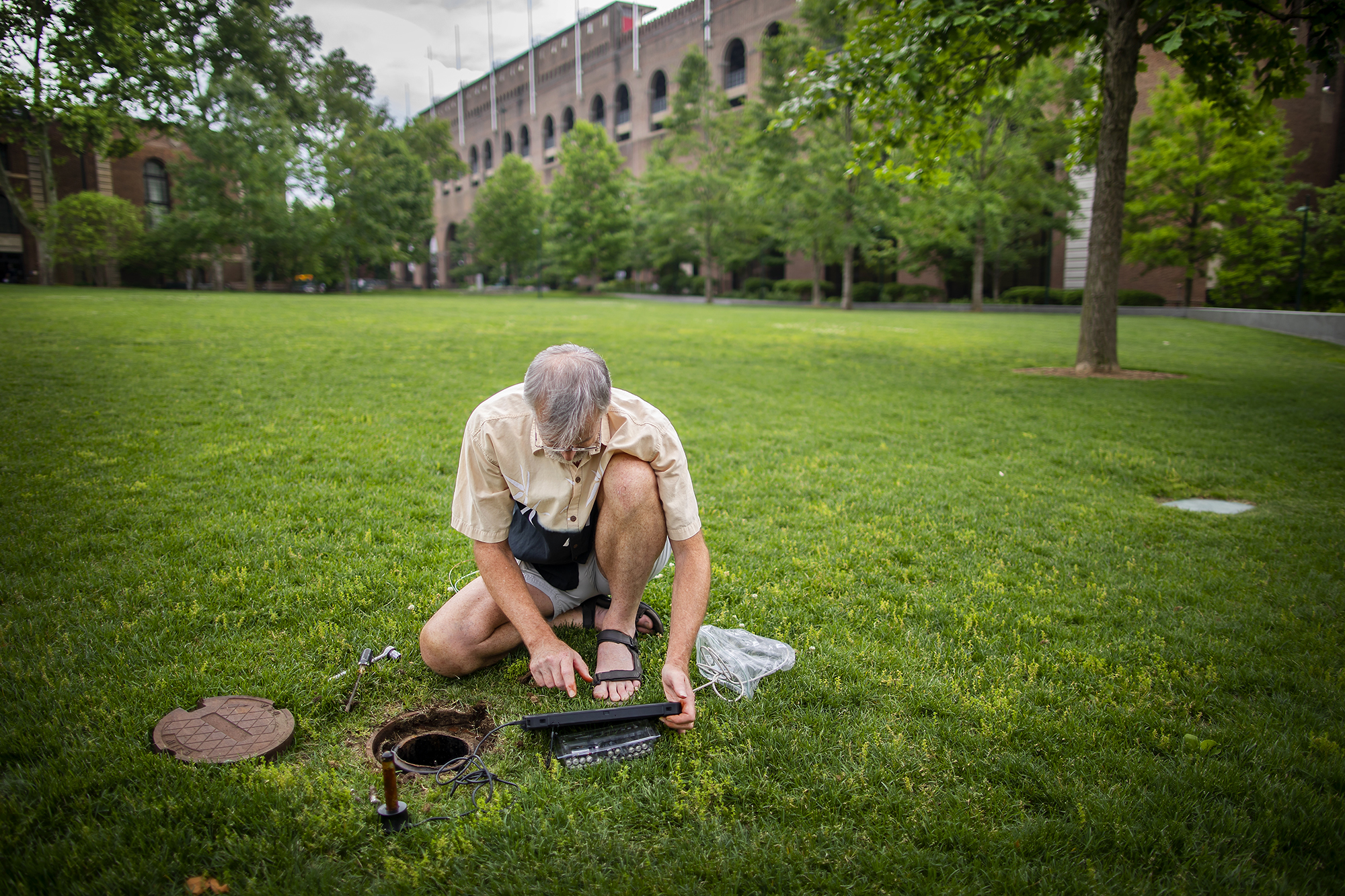 A scientist kneeling on a lawn checks a well using electronic monitoring equipment