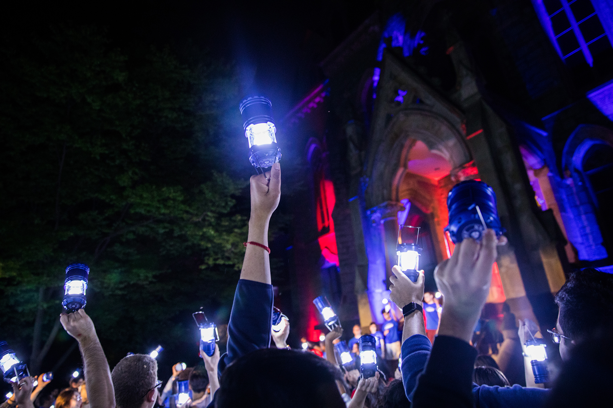 The crowd of students hold lanterns aloft in the night sky in front of College Hall.