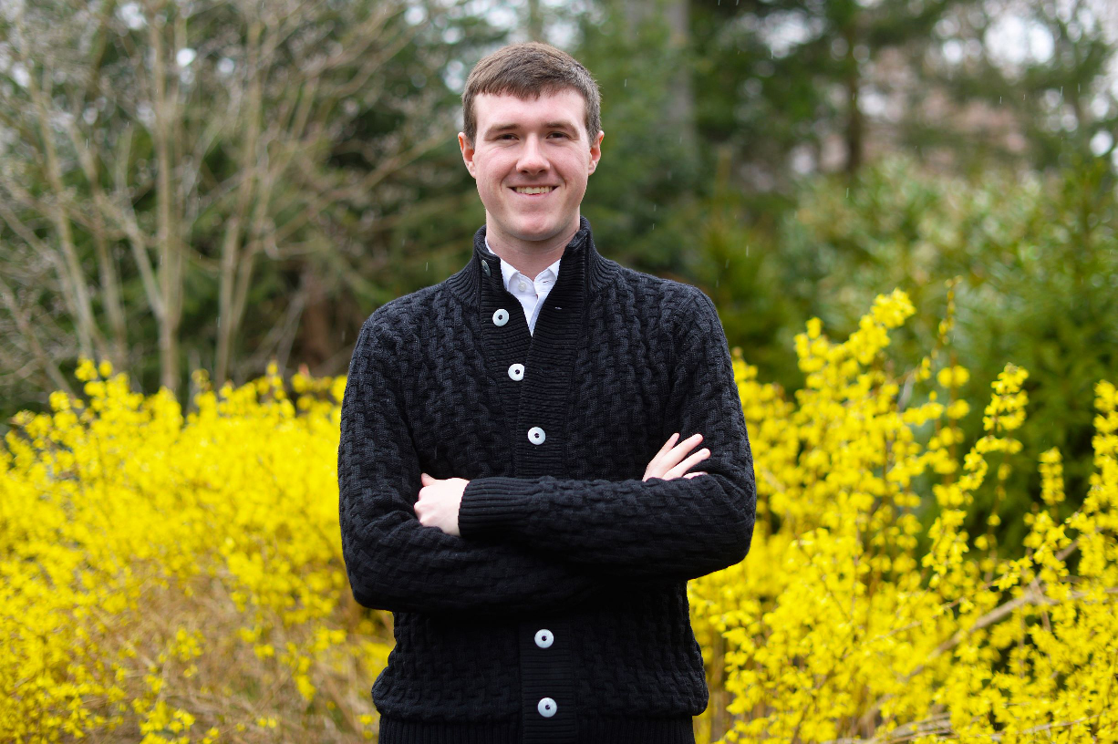 Student standing in front of a stand of forsythia. 