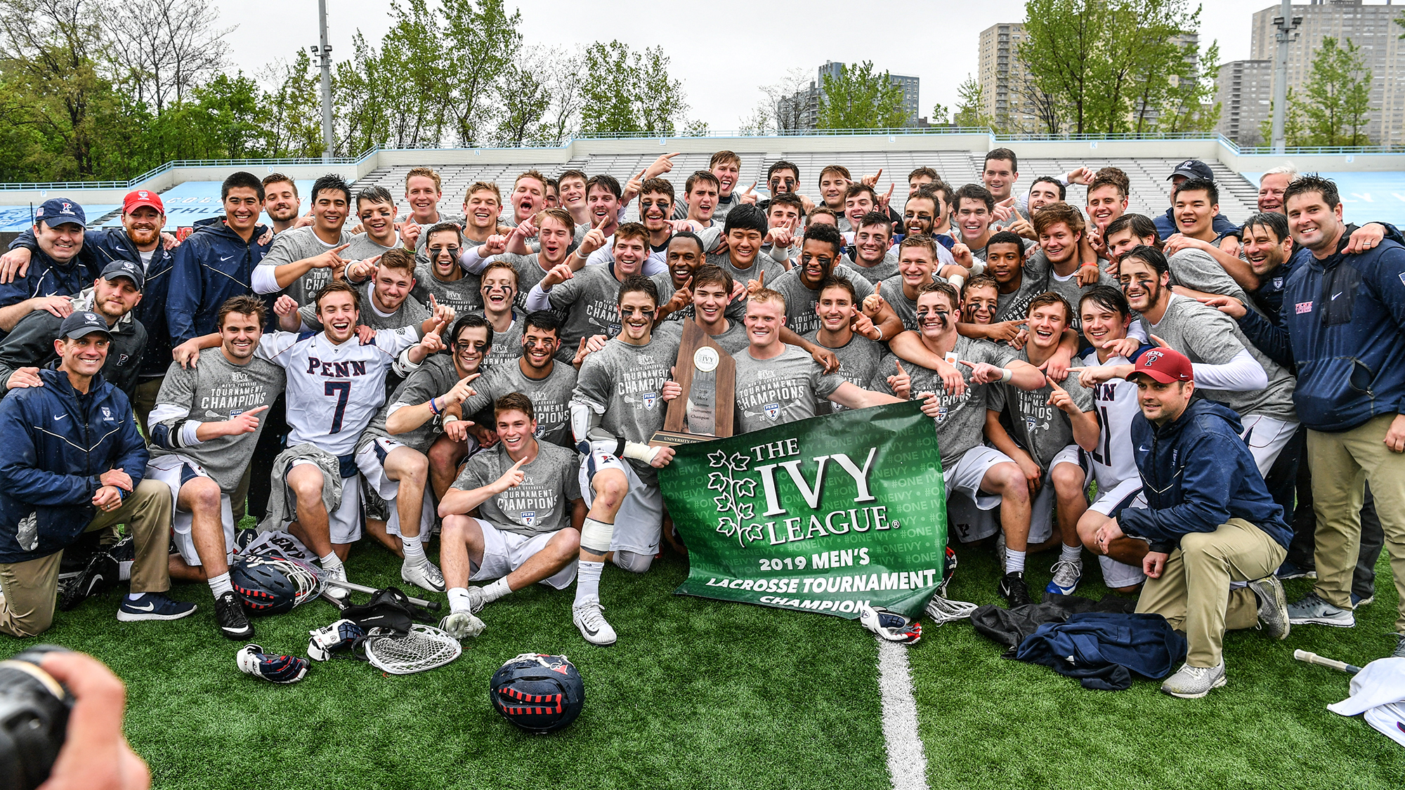 Men's lacrosse players hold up a championship banner on the field after beating Yale.