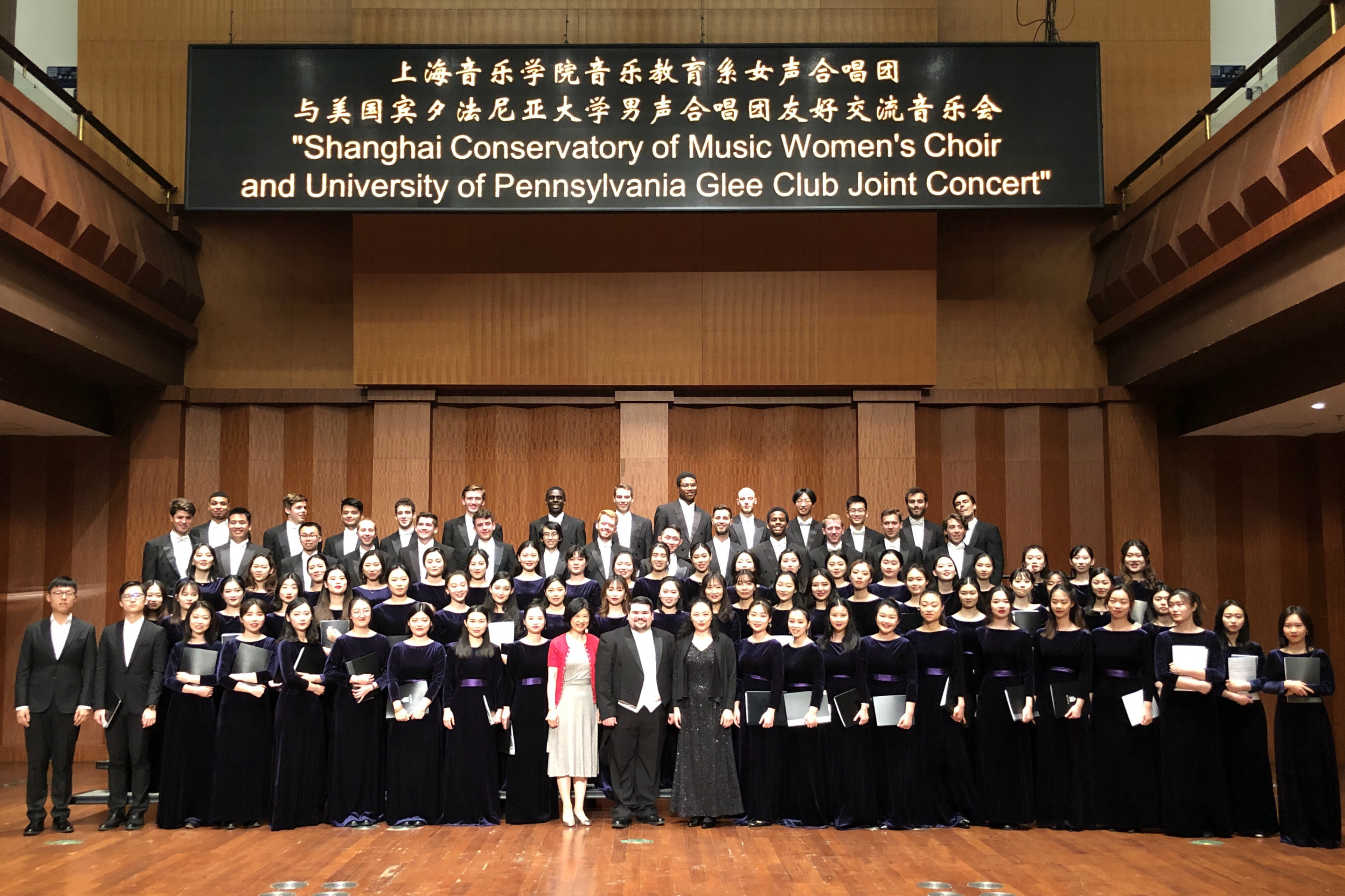 Concert with many people assembled on stage on risers dressed in formal attire. 