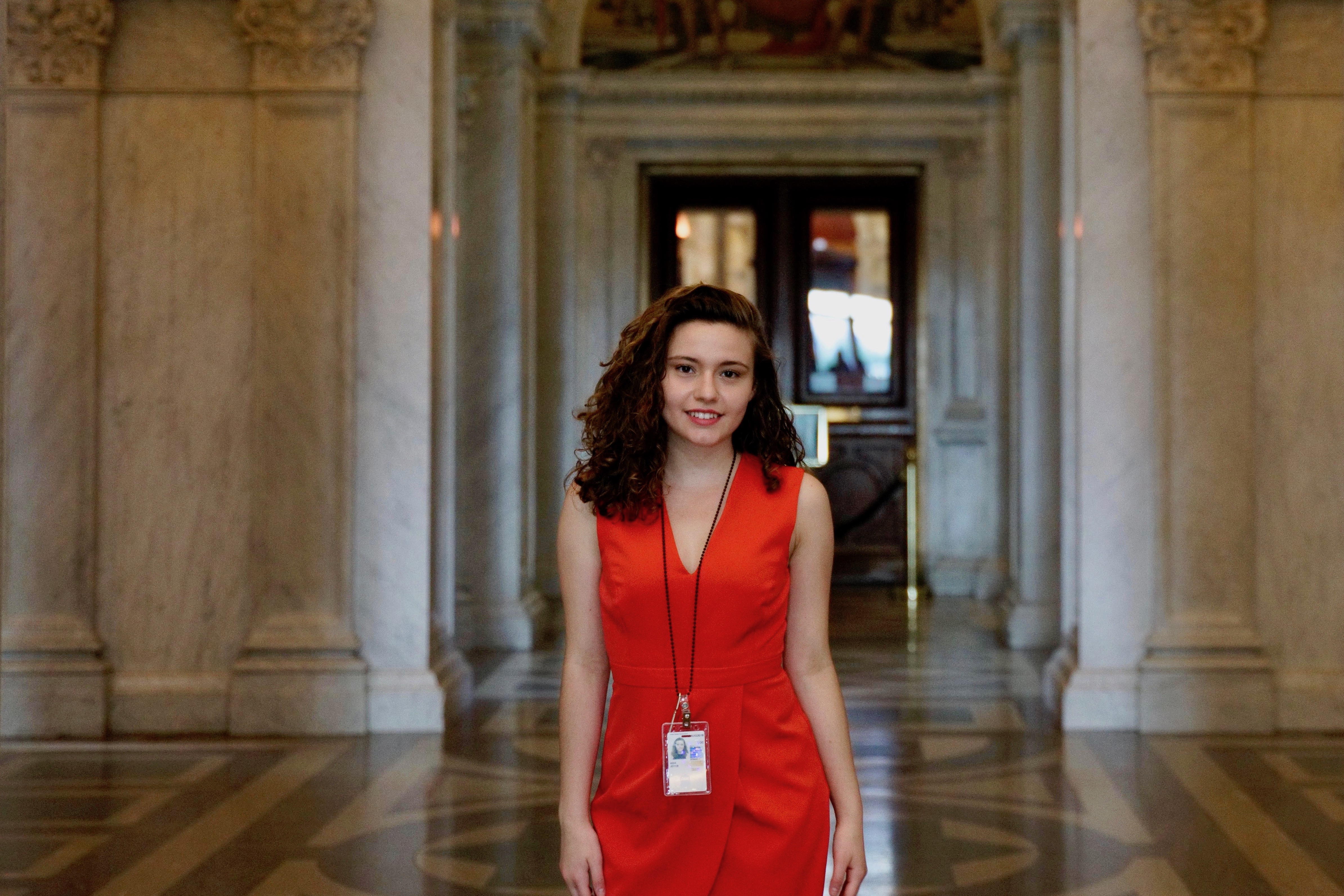 Student standing in lobby of marble building wearing an Identification badge.