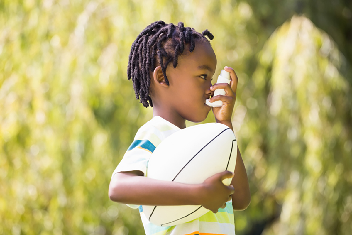 Young child outside in sunlight holding a ball and using an asthma inhaler