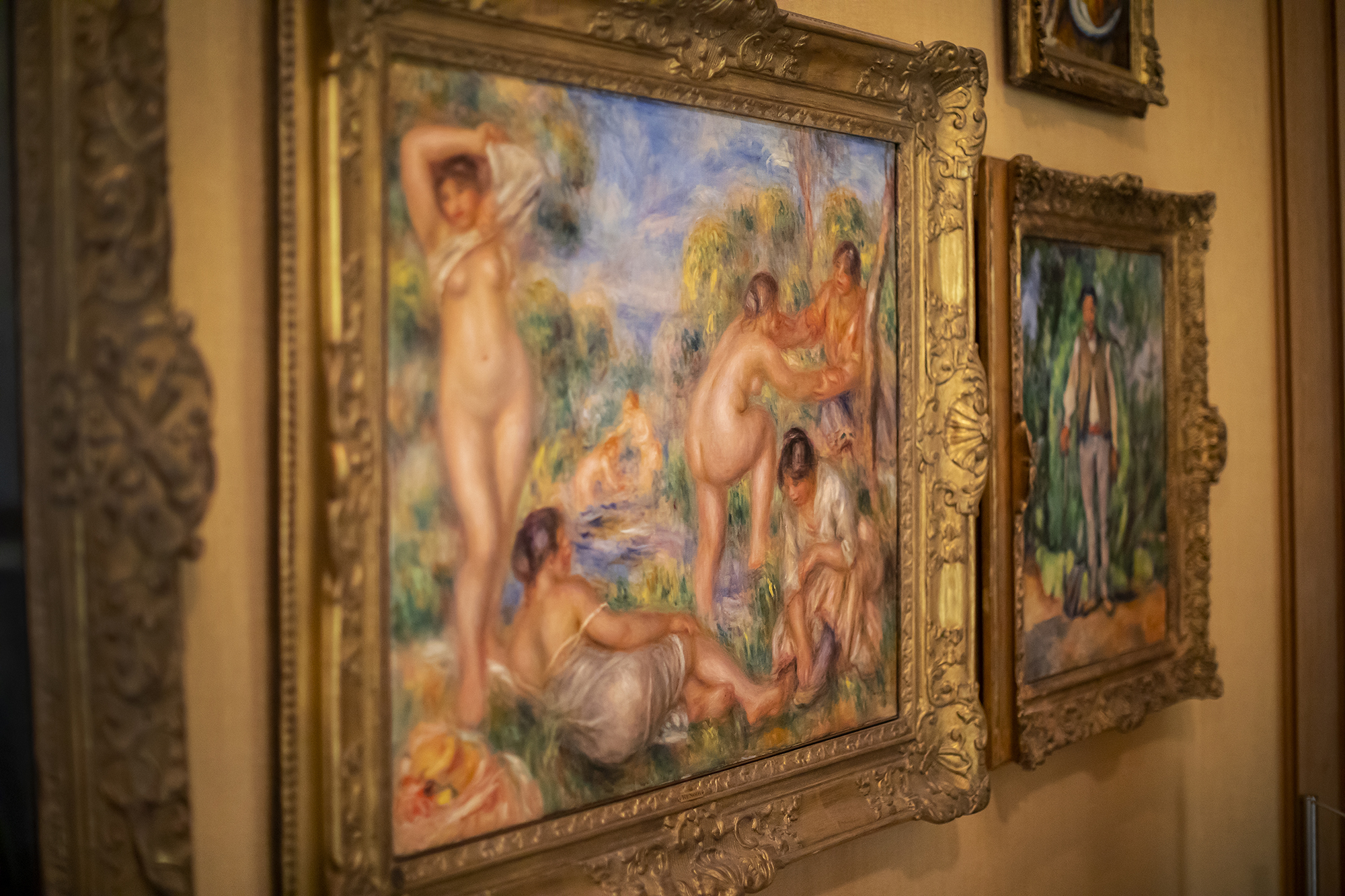 A Renoir painting of women, some nude, some dressed, in a blue and green landscape.