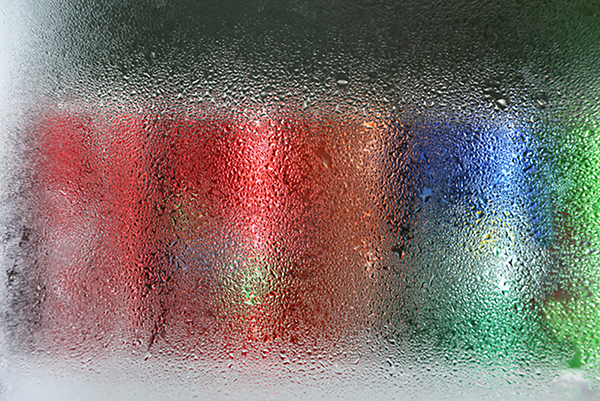cans of soda on a cooler shelf with condensation on the glass of the door.