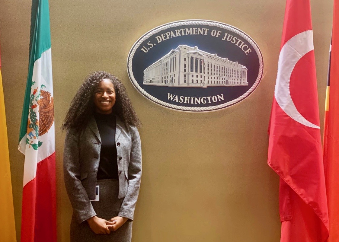 Student standing in front of plaque that says U.S. Department of Justice Washington, and flanked by two flags. 