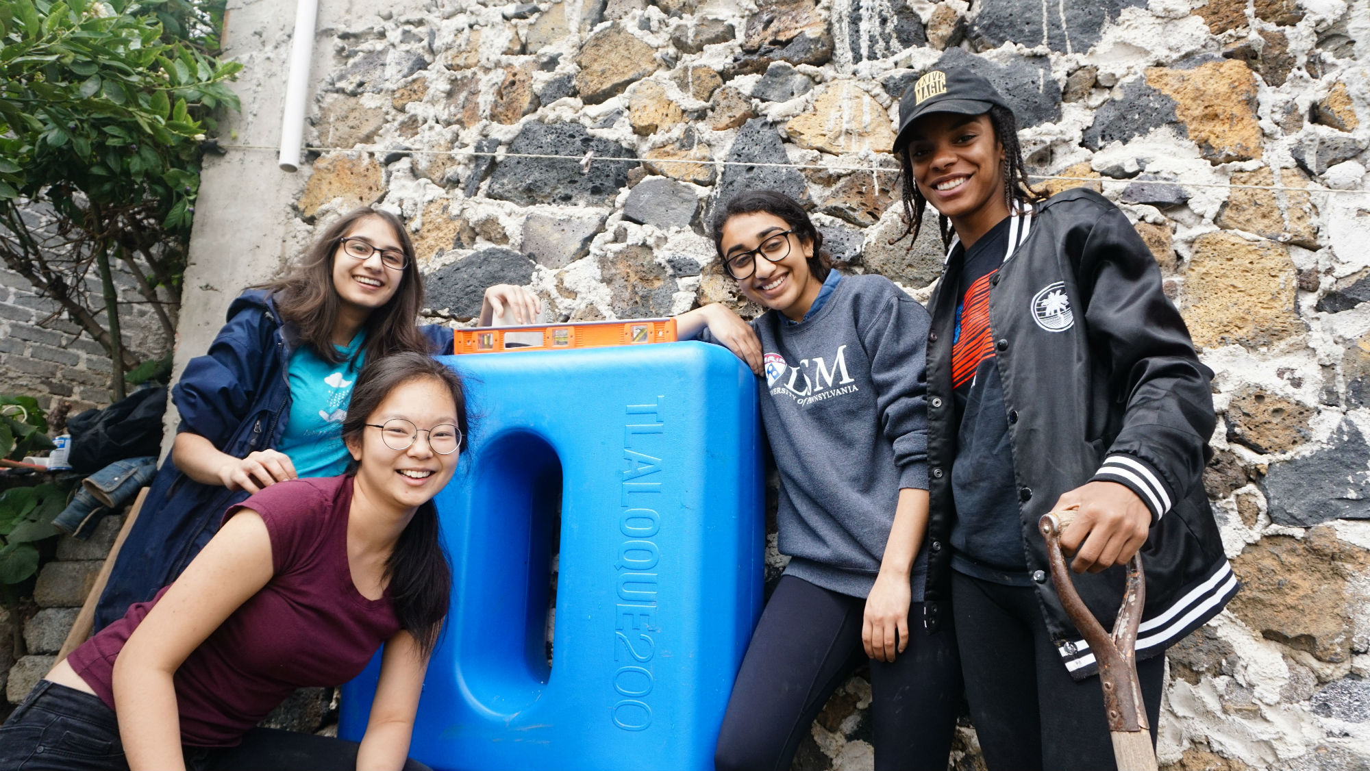 Four smiling students posing by a blue container with a level on top of it