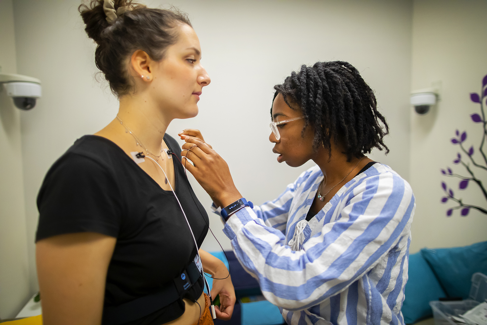 A young woman (right) places electrodes on another young woman's neck (left).