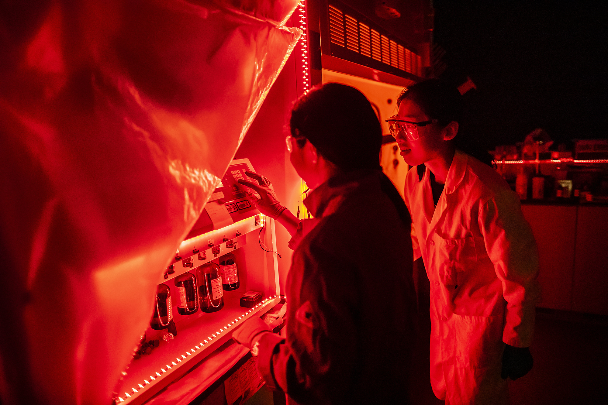 two students work in a chemistry lab lit by red light