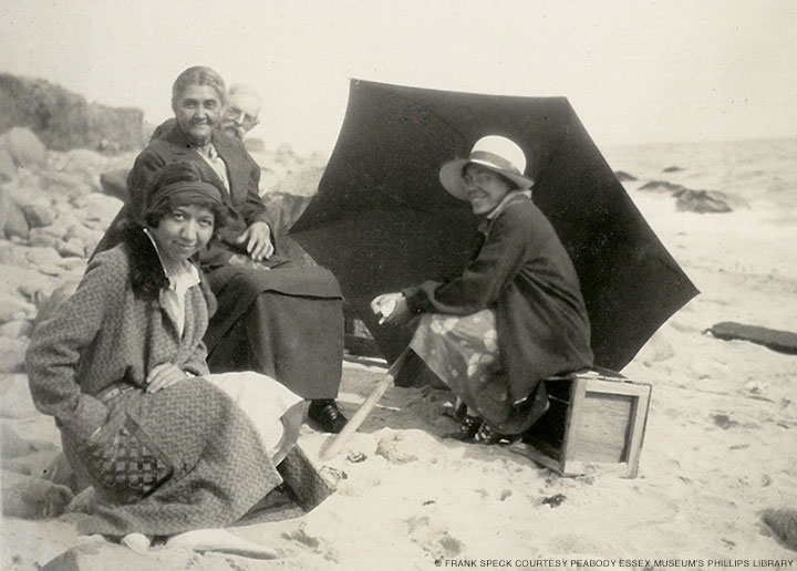 Gladys Tantaquidgeon seated on a beach with four other people and a black umbrella on the ground.