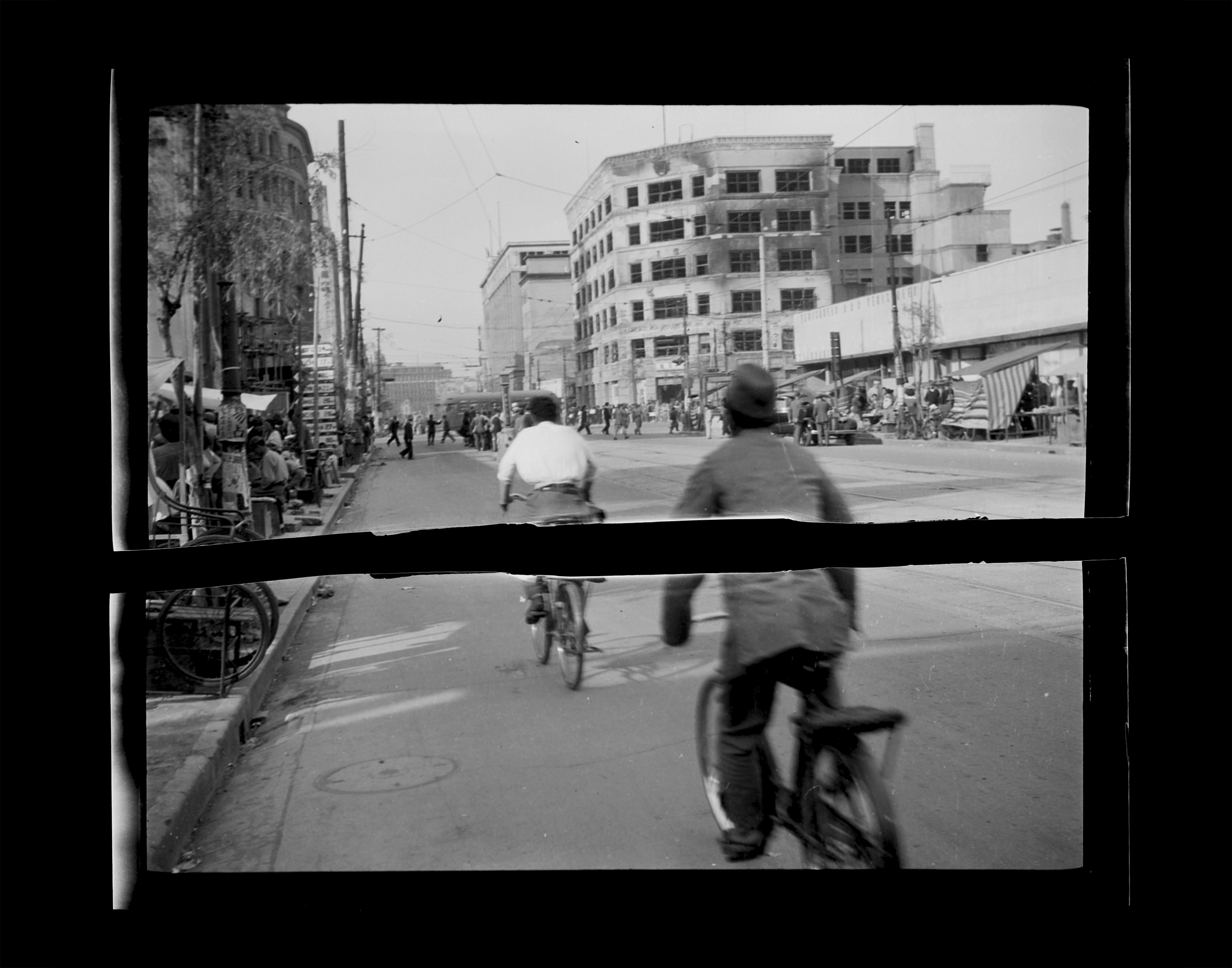 A black-and-white 1940s photograph of people riding bikes down a street