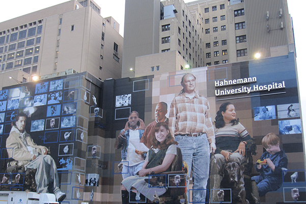 Front facade of Hahnemann Hospital with large murals of patients standing and sitting and in wheelchairs and a toddler.