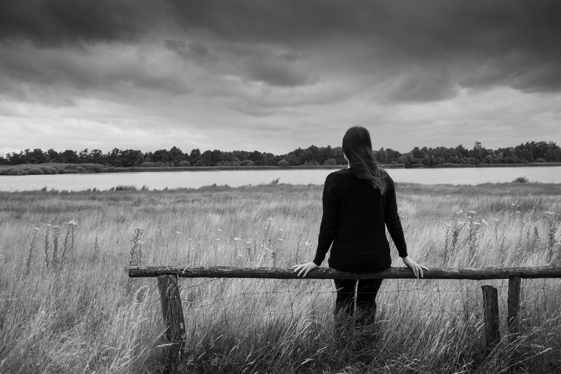 Black and white image of a person on a fence in front of a field. 