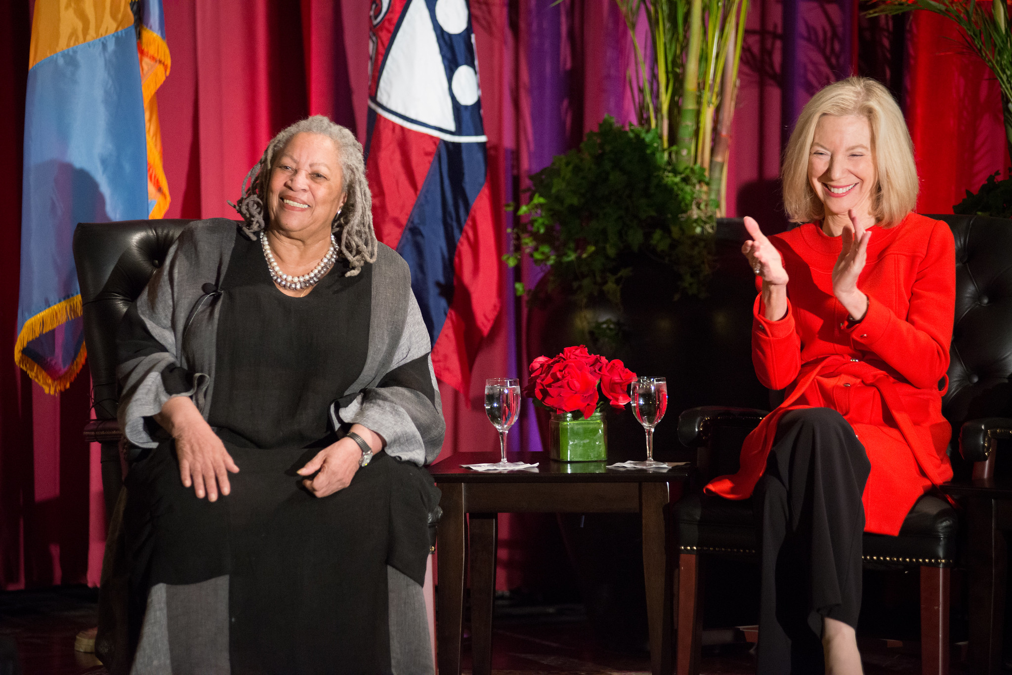 Amy Gutmann and Toni Morrison seated on stage with flags behind them