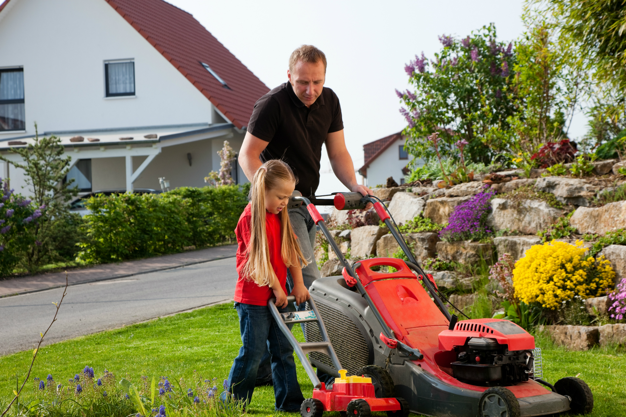 Parent teaching child how to mow grass