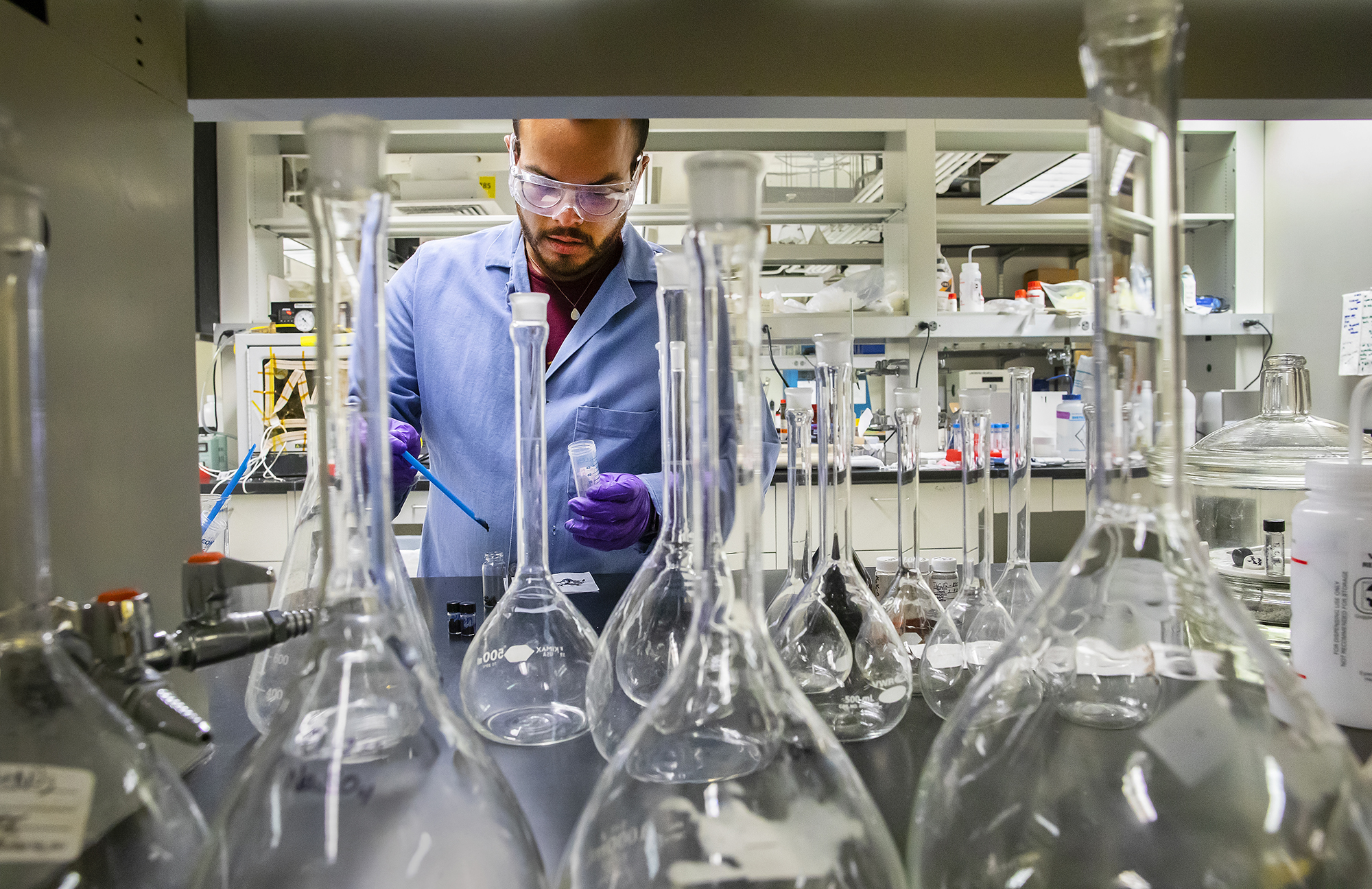 luis de jesus baez in a lab from a perspective taken behind a collection of flasks