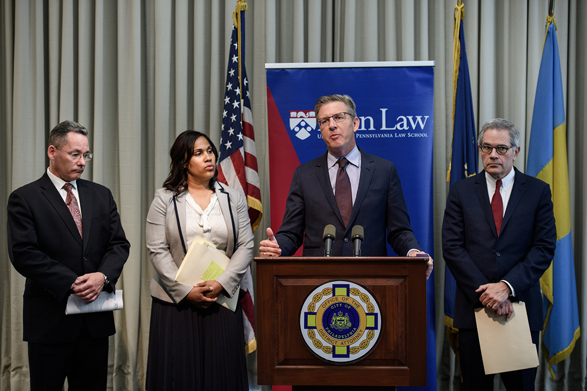 Four people at a press conference, third from left John Hollway speaking at podium, far right is DA Larry Krasner, beside Hollway is Keir Bradford-Grey.