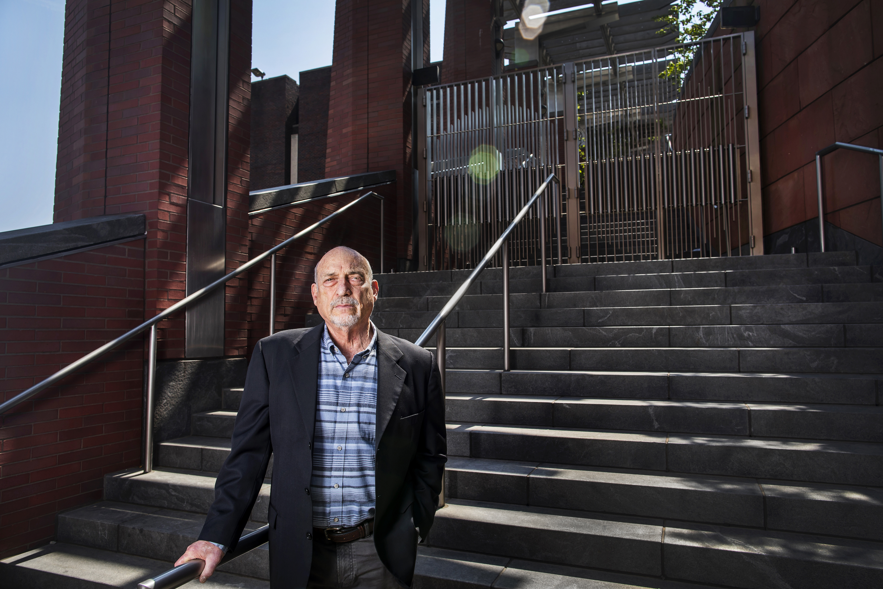 A person standing at the foot of a set of outdoor stairs, with a brick wall behind and fencing atop the stairs.