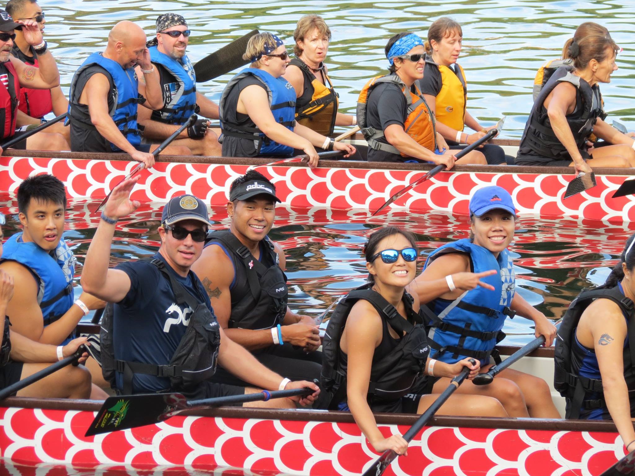 Paddlers in bright red boats on the water, smiling and posing for the camera.