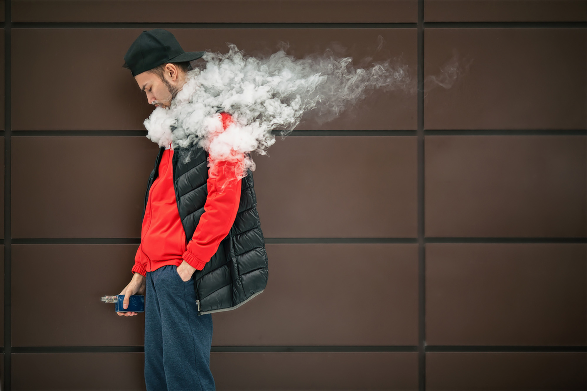 Side-view of person against a wall exhaling smoke from an e-cigarette