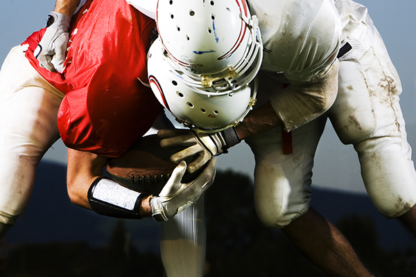Two football players bent over a football with helmets in contact, potential for concussion.