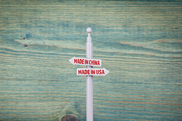 Two signposts, one reads Made in China, pointing left, directly beneath it reads Made in USA, pointing right, symbolic of the U.S. China trade war crossroads.