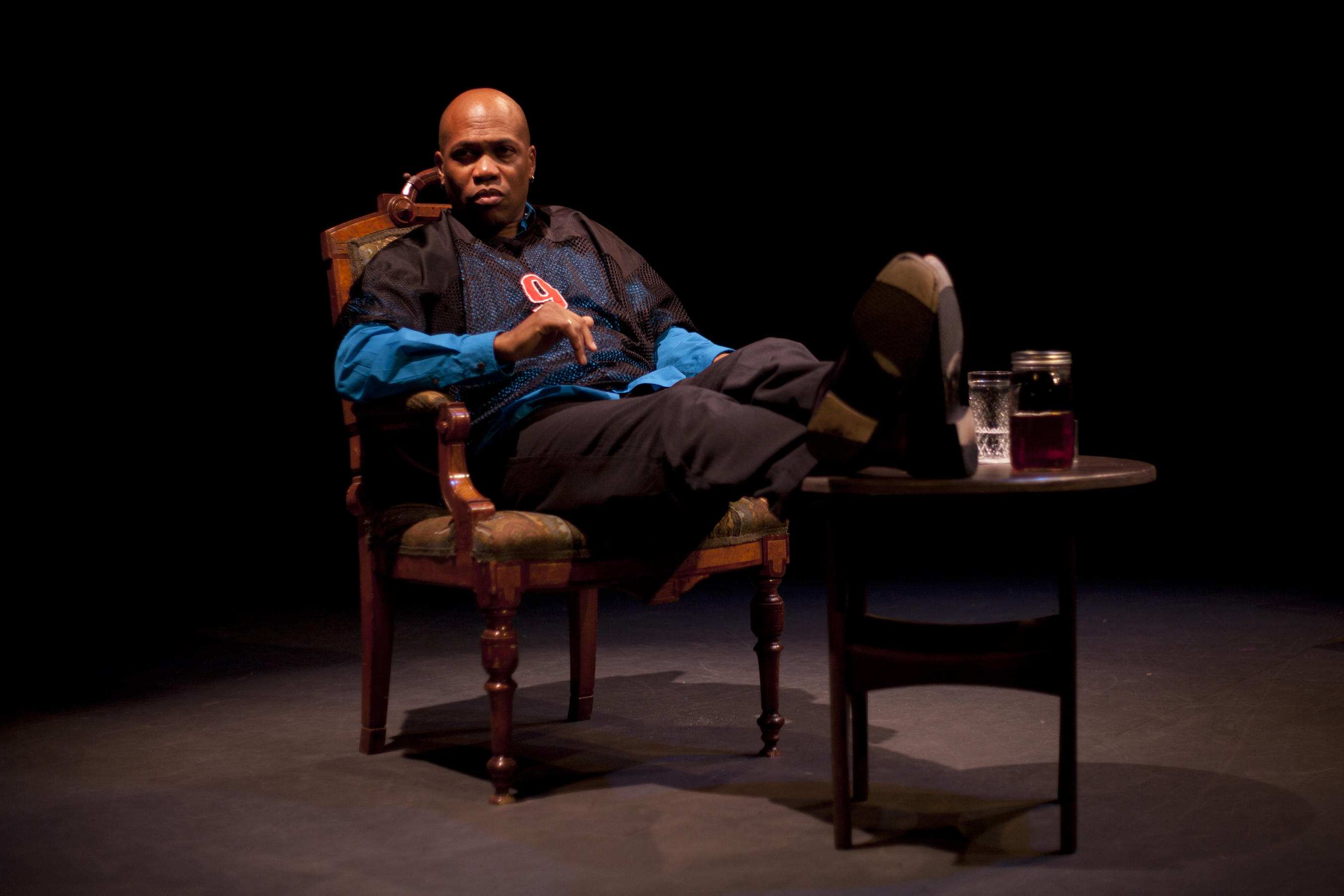 African American person sitting in a wooden chair, feet up on a wooden table that holds a ball jar filled with sweet tea.