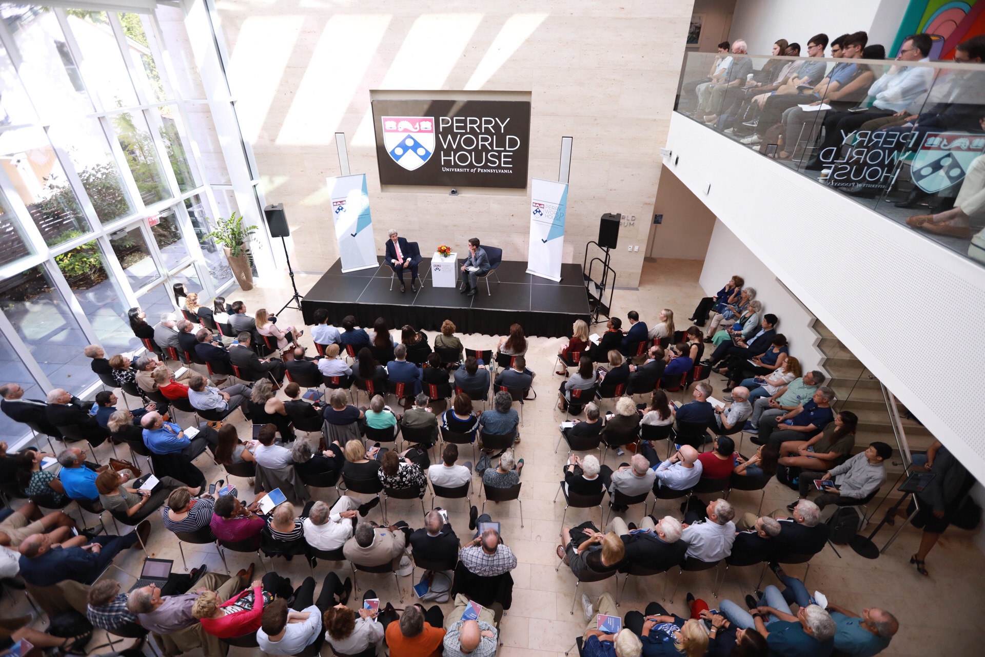 A large seated crowd at the Perry World House watches a discussion with John Kerry on stage.