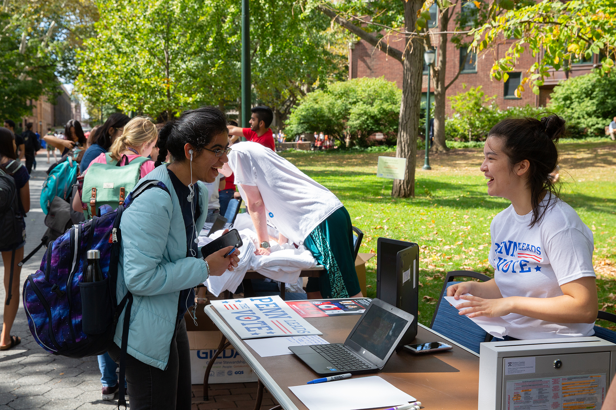 A volunteer with Penn Leads the Vote talks with a student outside on College Green